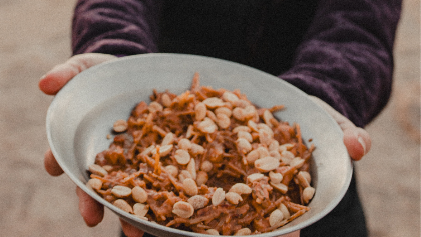 A close up shot of a person holding a ceramic bowl filled with Pad Thai topped with peanuts