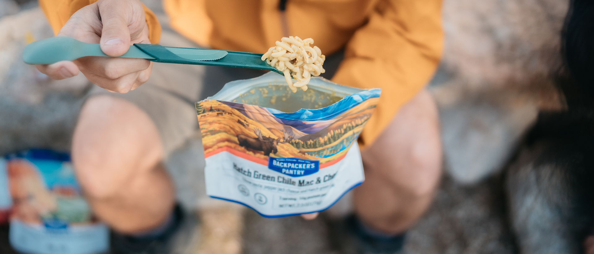 A person holding a spoon and eating Hatch Green Chile Mac and Cheese from the pouch