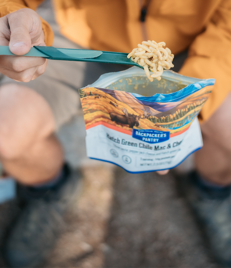 A person holding a spoon and eating Hatch Green Chile Mac and Cheese from the pouch